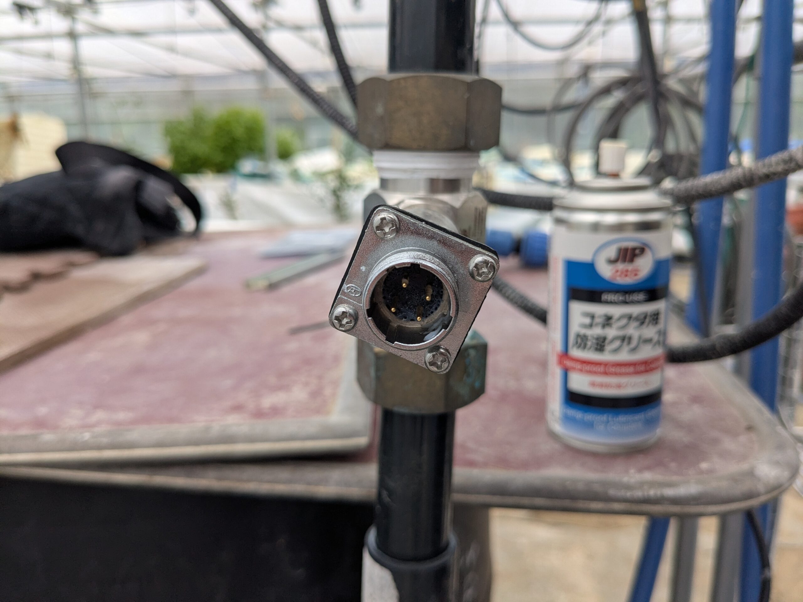 センサー側の4本の金属ピンに防湿グリースが薄く乗った状態。奥にコネクタ用防湿グリースのスプレー缶